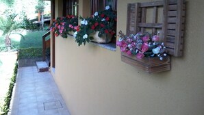 Een gevel met een overdekte veranda, planten in potten met bloemen en een houten luik.