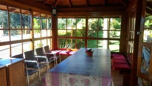 Een overdekte eethoek met een lange tafel, stoelen en banken.