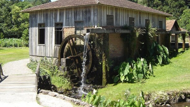 Een rustiek houten gebouw met een groot waterrad en een fundering van baksteen.