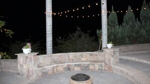 An outdoor patio area with stone steps, a fire pit, string lights, and potted plants.