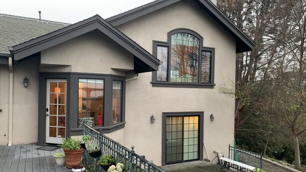 A two-story house with a balcony, large windows, and potted plants.