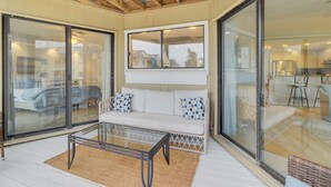 Un vaste espace de vie comprenant un canapé blanc, une table basse en verre et une grande porte-fenêtre coulissante donnant sur un balcon.