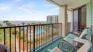 Un balcon avec vue sur une piscine et une plage, aménagé avec des chaises et une table.