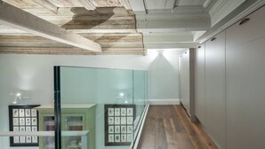 Een gang met een houten vloer, een glazen scheidingswand met ingelijste foto’s en een witte muur met een lamp.