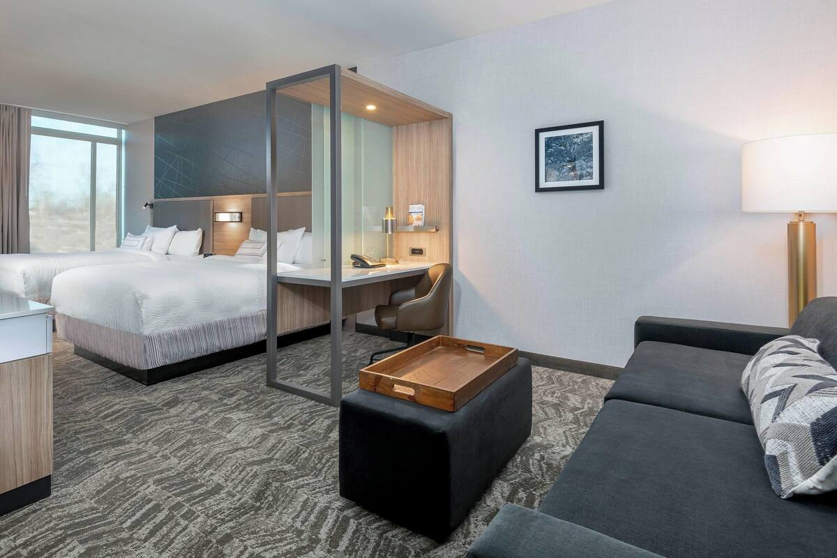 Habitación de hotel con una cama grande, un escritorio, una silla, un sofá y una pequeña bandeja de madera sobre un otoman.