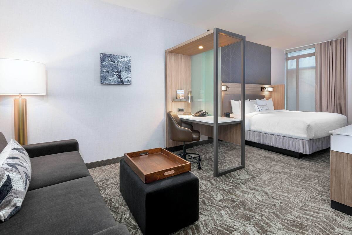 Una habitación de hotel con cama, escritorio, silla, sofá y una pequeña mesa de madera.