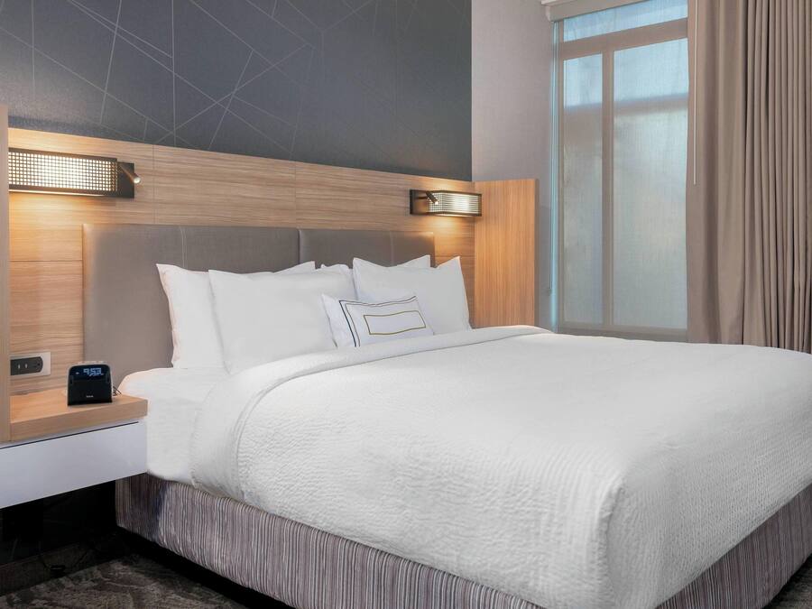 Une chambre d’hôtel moderne avec un grand lit, une table de chevet avec une lampe et une fenêtre avec des rideaux.