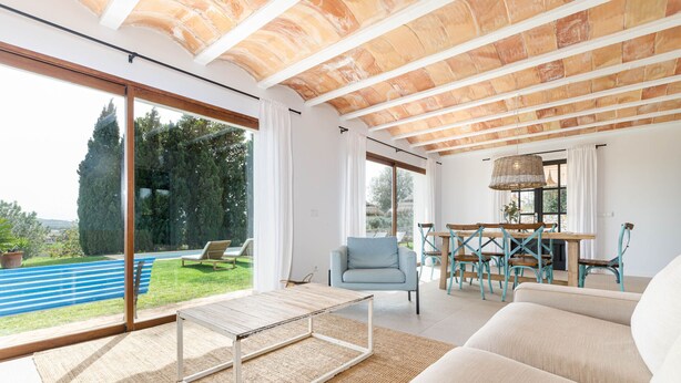 Amplia sala de estar con un gran ventanal que da a una piscina, techo de madera y un juego de comedor.