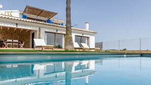 Una casa moderna con piscina, un patio con sillones de descanso y fachada de piedra.
