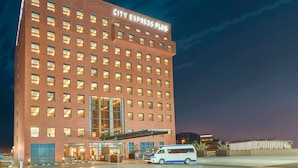 A tall brick building with a large entrance and a van parked in front. - City Express Plus by Marriott Tijuana (Tijuana)