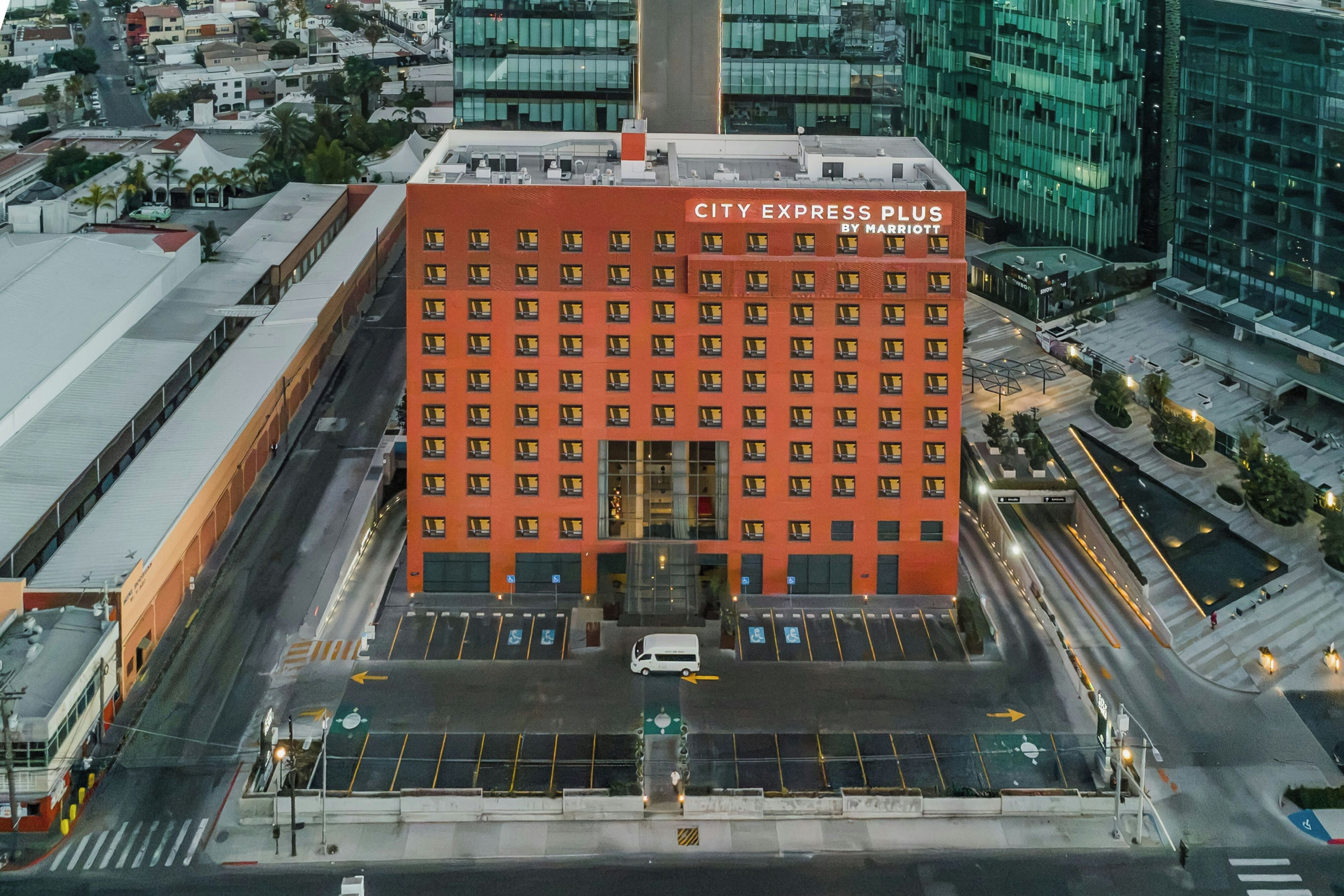 A multi-story building with a red facade, multiple windows, and a parking lot in front.