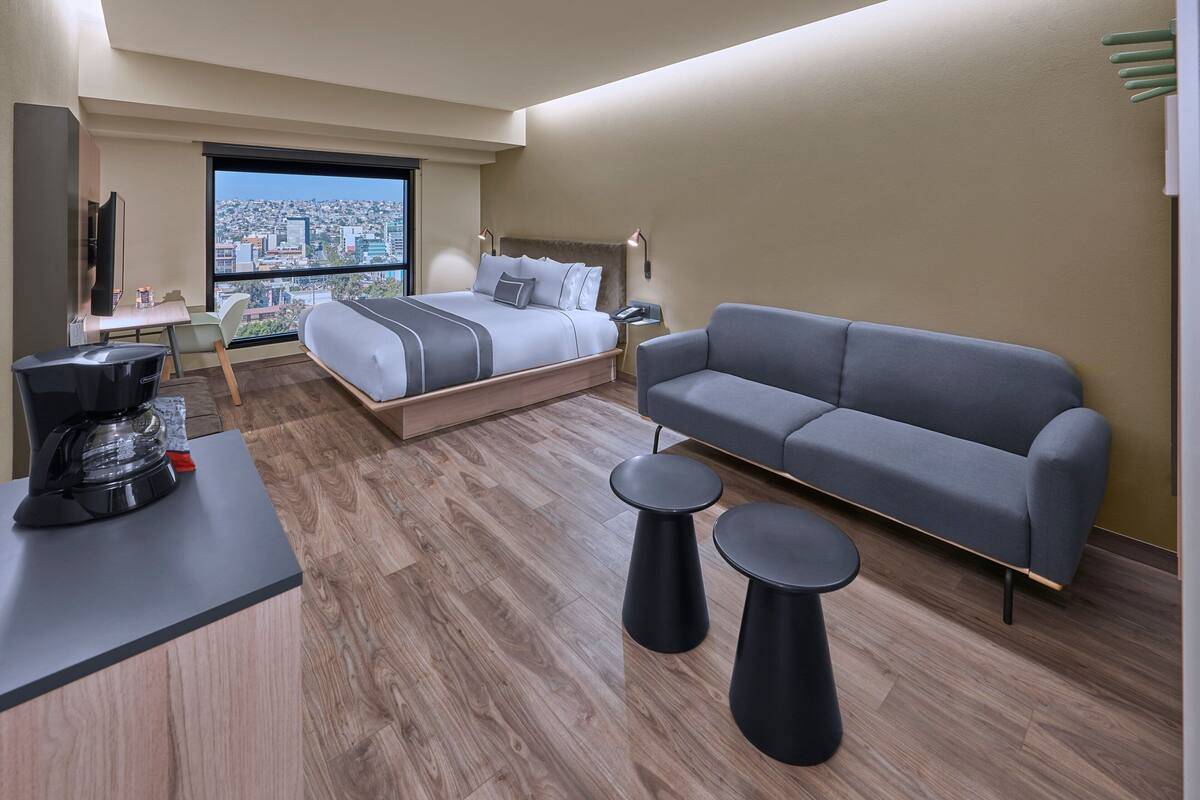 Una habitación de hotel moderna con una cama, un sofá gris, una máquina de café y un escritorio con una silla.
