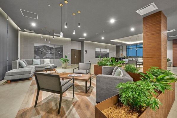 A modern lounge area with sofas, chairs, and a coffee table, featuring a large wooden planter with plants. - City Express Plus by Marriott Tijuana (Tijuana)