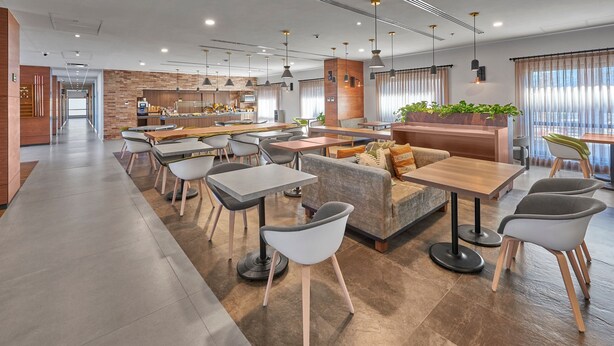 A modern dining area with multiple tables and chairs, a central seating area with a sofa, and a kitchen in the background. - City Express Plus by Marriott Tijuana (Tijuana)
