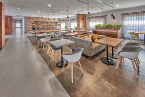 A modern dining area with multiple tables and chairs, a central seating area with a sofa, and a kitchen in the background. - City Express Plus by Marriott Tijuana (Tijuana)