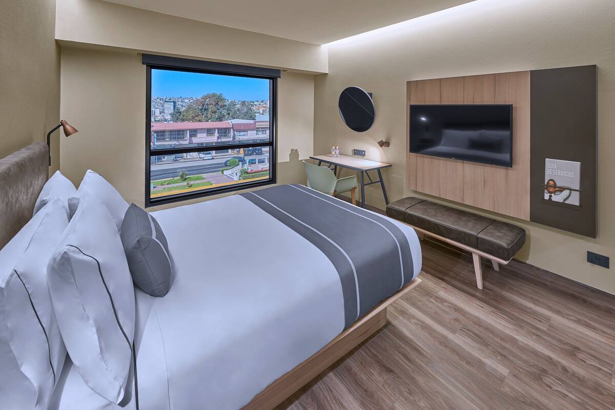 Una habitación de hotel moderna con una cama grande, un escritorio, un televisor y una ventana con vista a la ciudad.