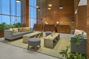 A modern lobby with a grey sofa, two grey ottomans, a coffee table, and a potted plant.