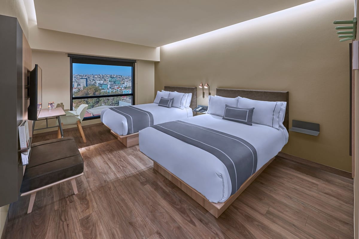 Habitación de hotel moderna con dos camas, un escritorio y un ventanal grande con vistas a la ciudad.