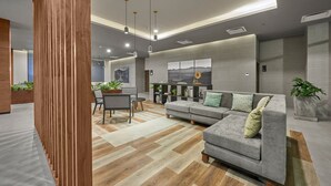 A modern living room with a grey sofa, wooden floor, and a dining area with a table and chairs. - City Express Plus by Marriott Tijuana (Tijuana)