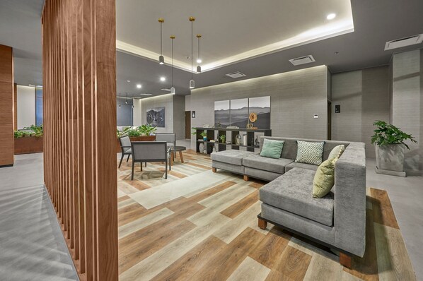Una sala moderna con un sofá gris, piso de madera y una zona de comedor con mesa y sillas.
