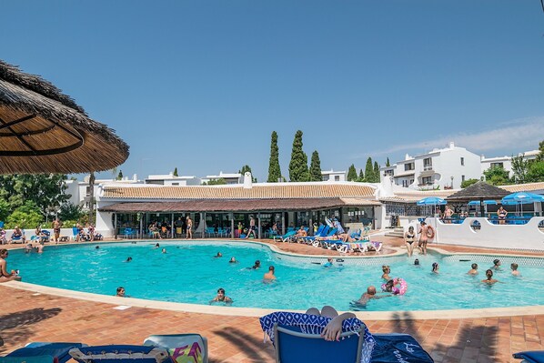 A swimming pool area with multiple pools, lounge chairs, and umbrellas.
