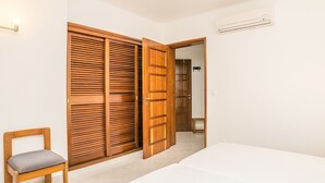 A bedroom with a wooden wardrobe, a small bedside table, and a chair. - Jasmine Apartment, AC, Pool, Balcony (Albufeira)