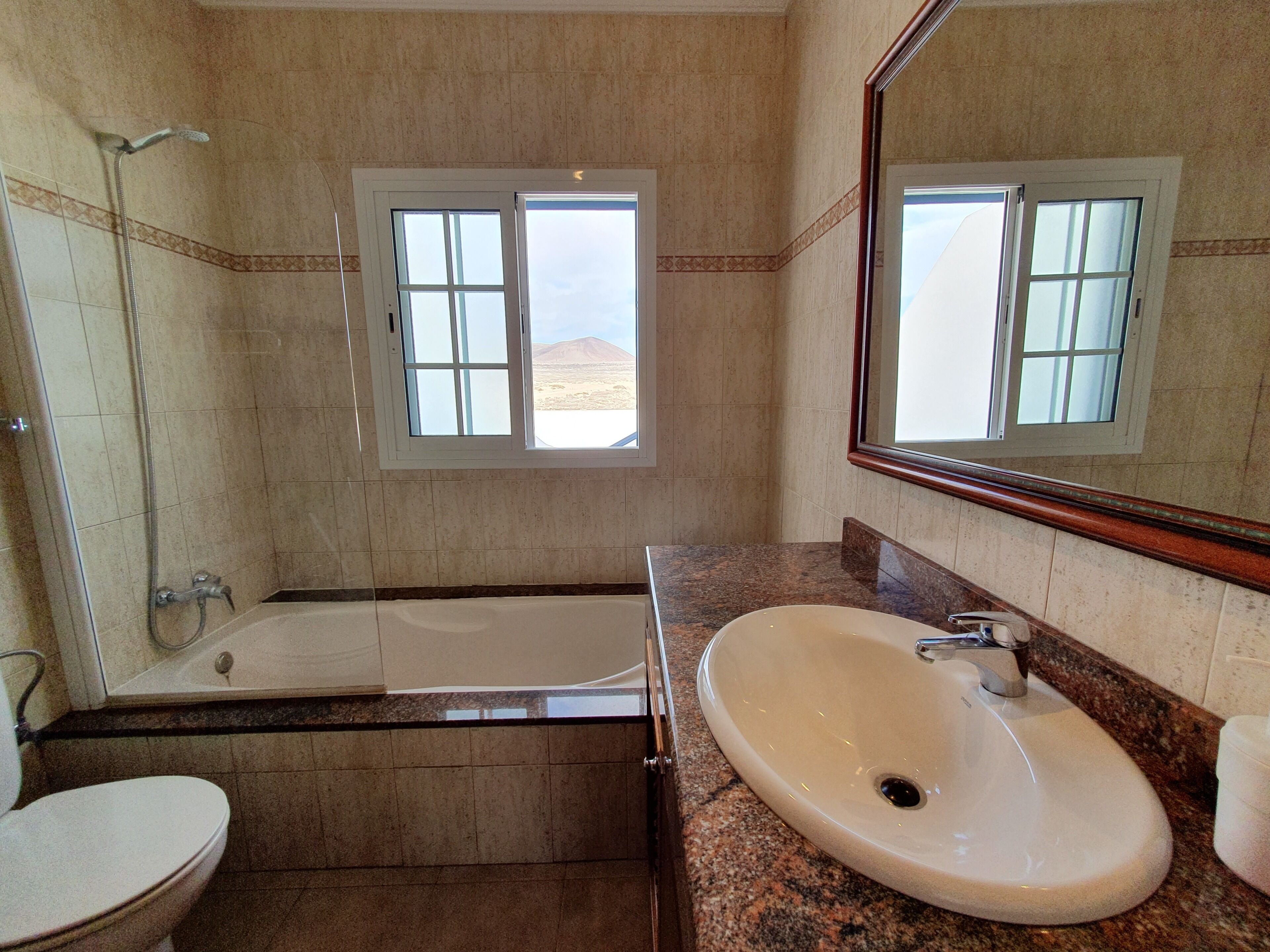 A bathroom with a bathtub, a sink, and a toilet. There is a window with a view of a desert landscape.