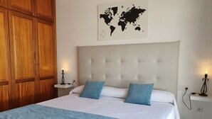 Una cama bien hecha con un edredón blanco y azul, dos almohadas a juego y un mapa del mundo en la pared de arriba.