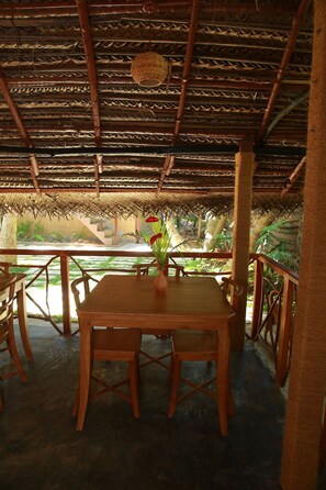 A wooden table with chairs and a vase of flowers on a covered patio with a thatched roof. - Lime Cabanas Sri Lanka (Koggala)