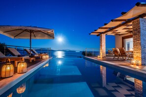A poolside area with lounge chairs and umbrellas, a clear view of the water, and stone pillars.