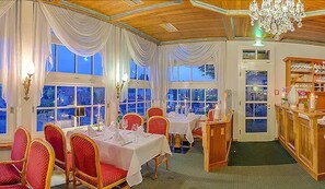 Un espace repas avec des tables disposées pour accueillir quatre personnes, des chaises à revêtement rouge et un lustre.