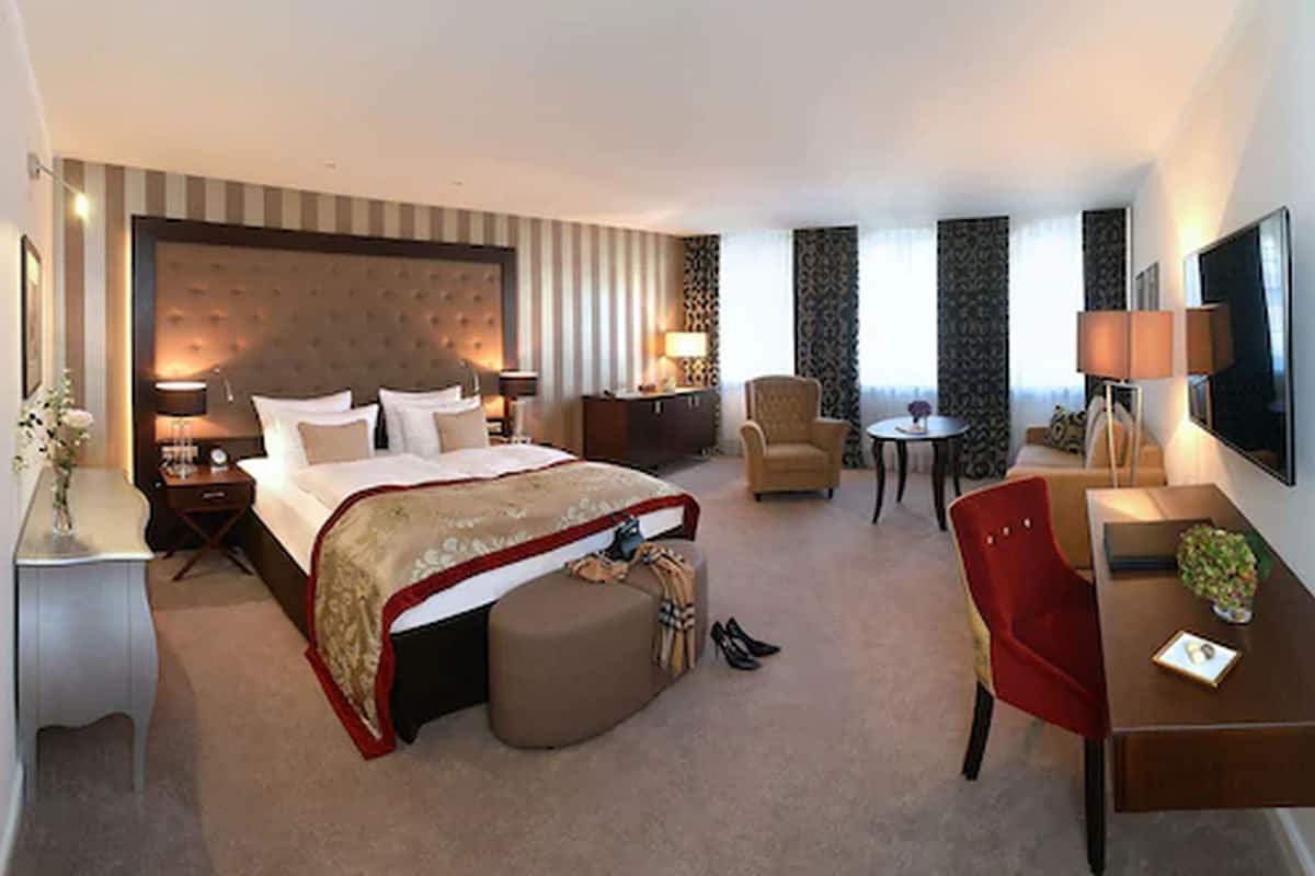 A hotel room with a large bed, a desk, a chair, a small table, and a TV.