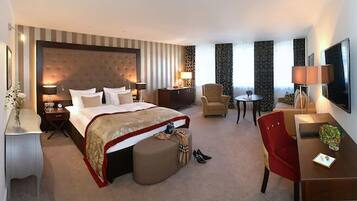 A hotel room with a large bed, a desk, a chair, a small table, and a TV.