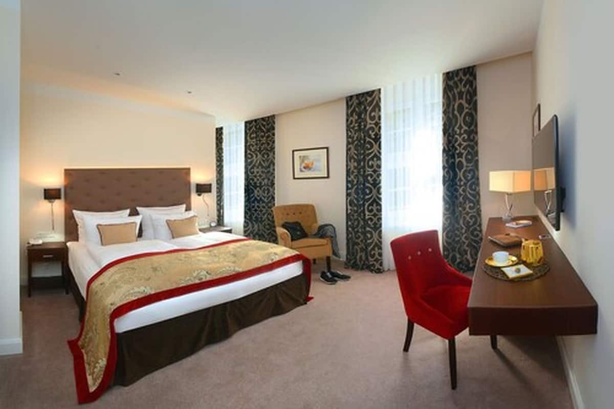 A hotel room with a large bed, a desk, a chair, and a TV.