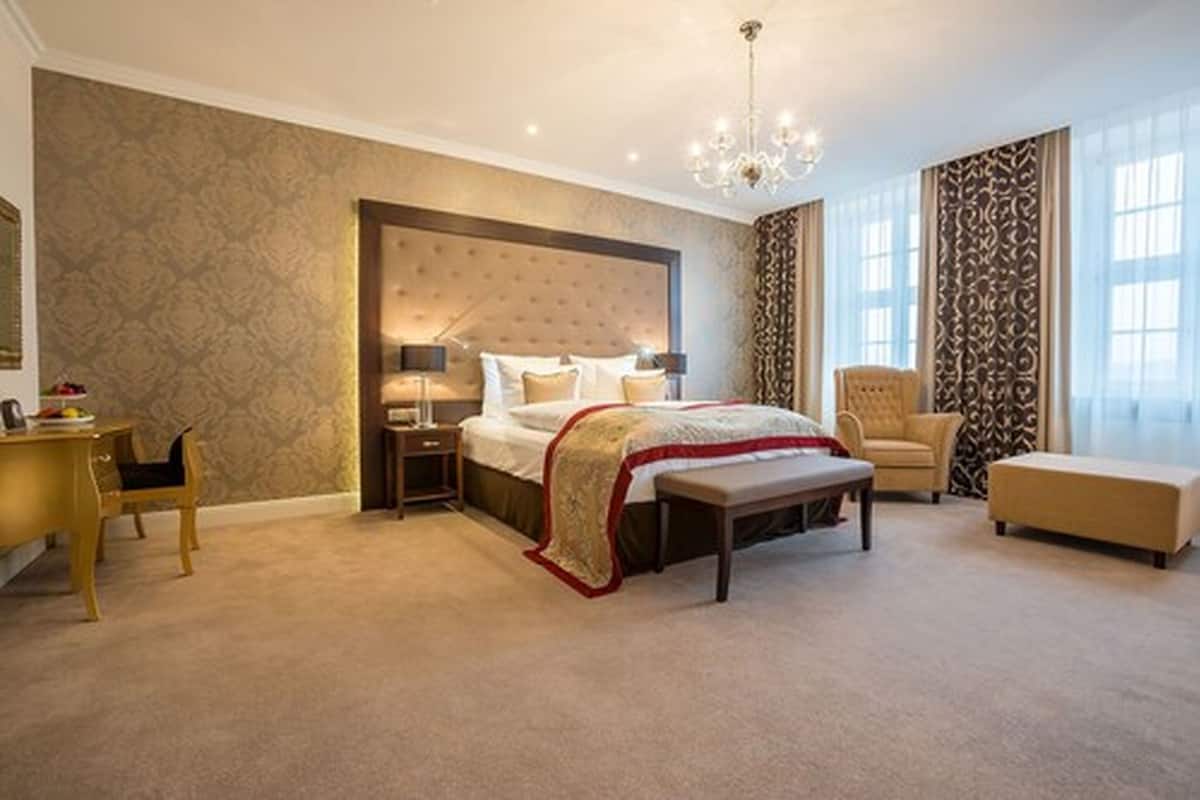 A bedroom with a large bed, bedside tables, a chair, a desk, and a chandelier.