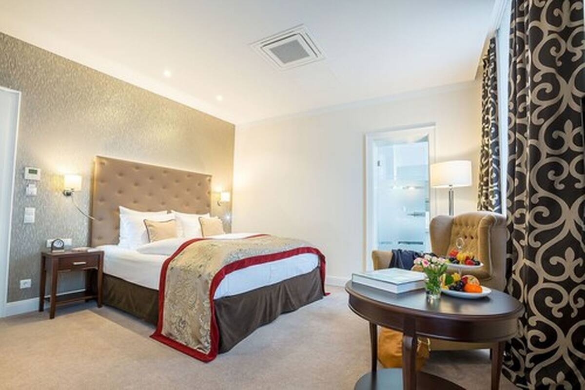 A hotel room with a large bed, bedside tables, a desk with a chair, and a view of the outside.