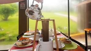A hand pouring tea from a floral teapot onto a wooden stand. - Nafre House (Monteverde)