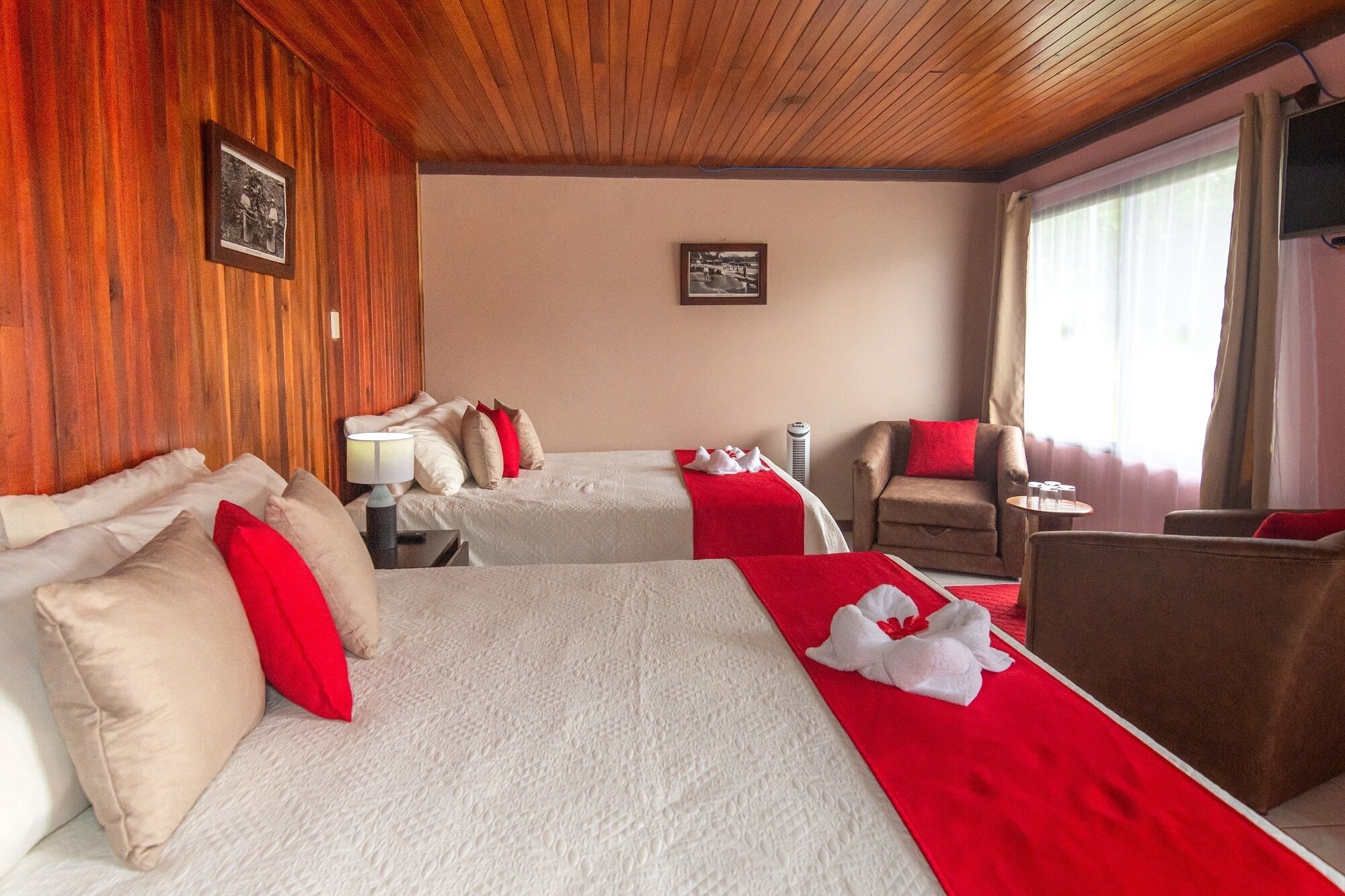A hotel room with two beds, a sofa, a small table, and a window with curtains.