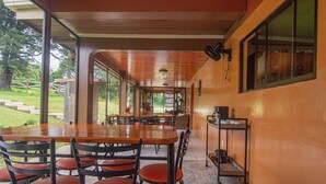 A spacious indoor dining area with wooden tables and chairs, large windows, and a view of the outdoors. - Nafre House (Monteverde)
