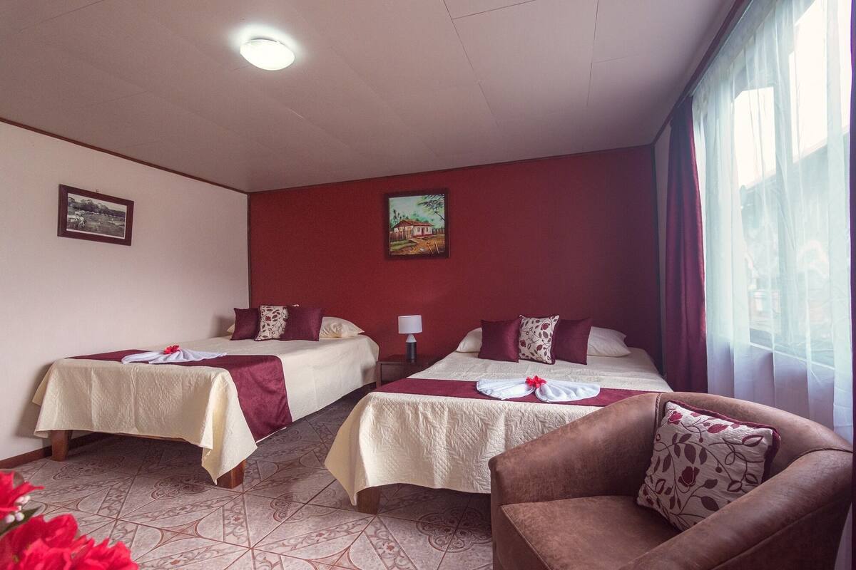 A hotel room with two beds, a sofa, a painting on the wall, and a window with curtains.