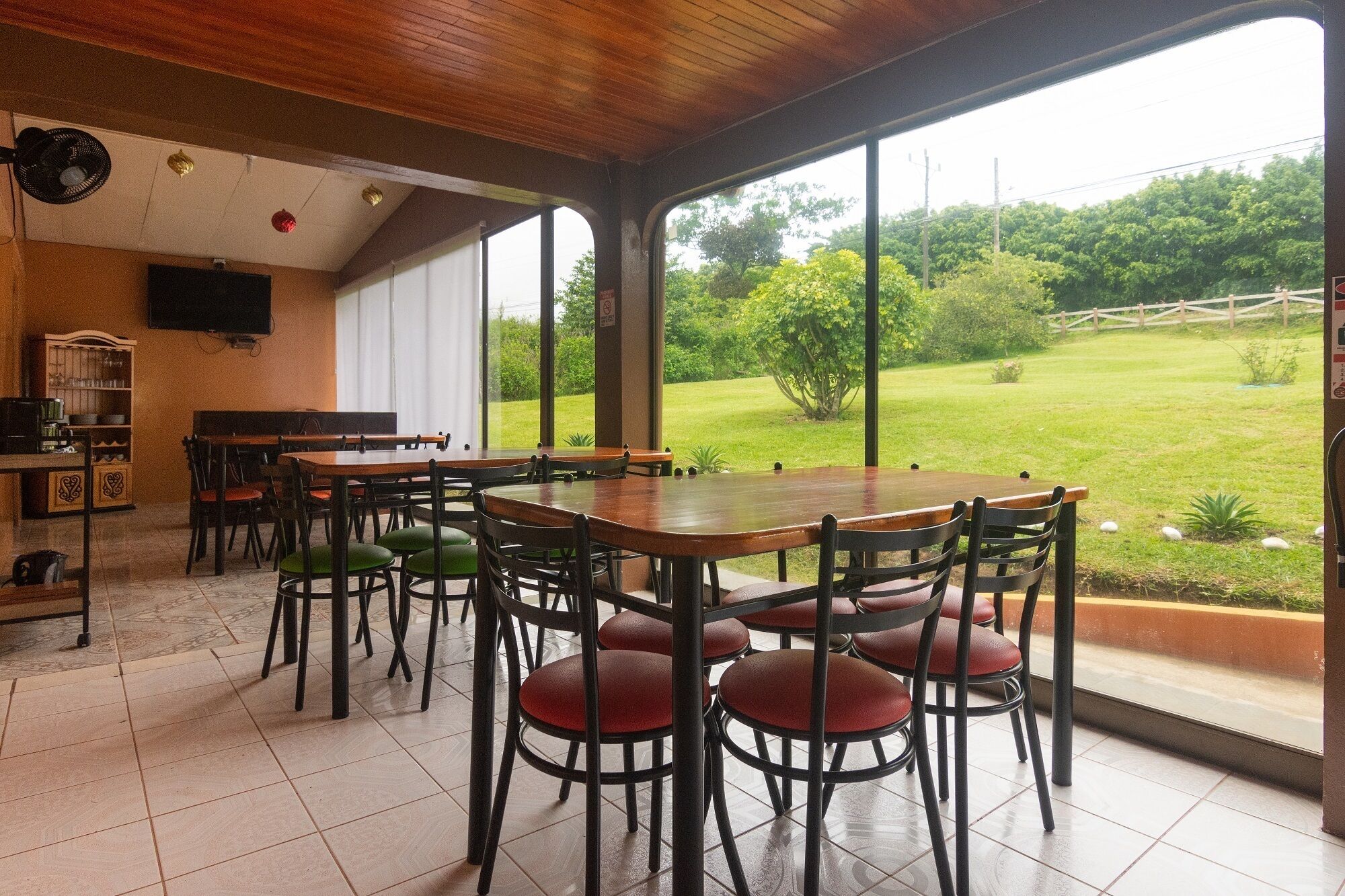 A dining area with a large table and chairs, a television, and a view of a grassy landscape through large windows.