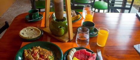 A wooden dining table with plates of food, a teapot, and glasses of water and orange juice.