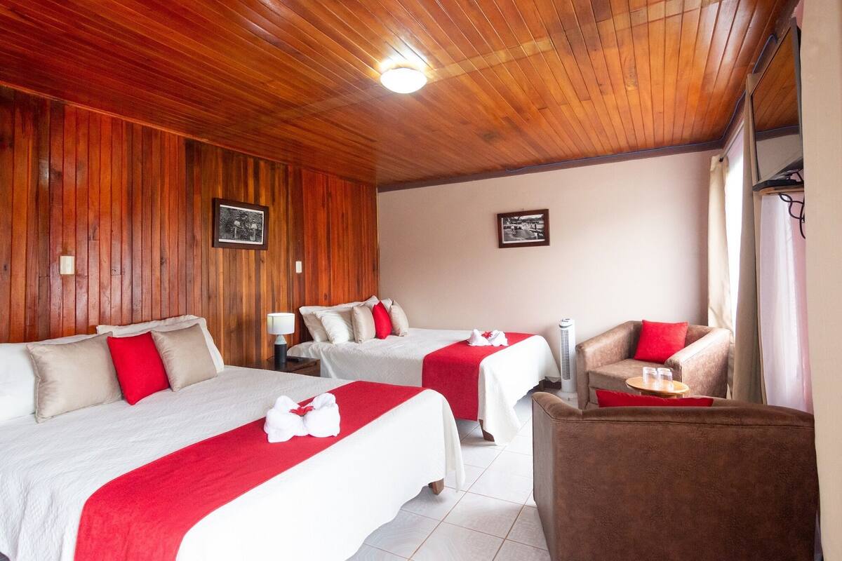 A hotel room with two beds, a wooden ceiling, and a small seating area with a chair and table.