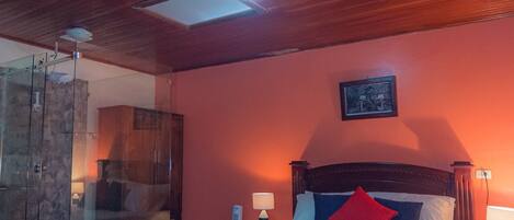Un dormitorio con techo de madera, cabina de ducha de vidrio, cama con almohadas e imagen enmarcada en la pared.
