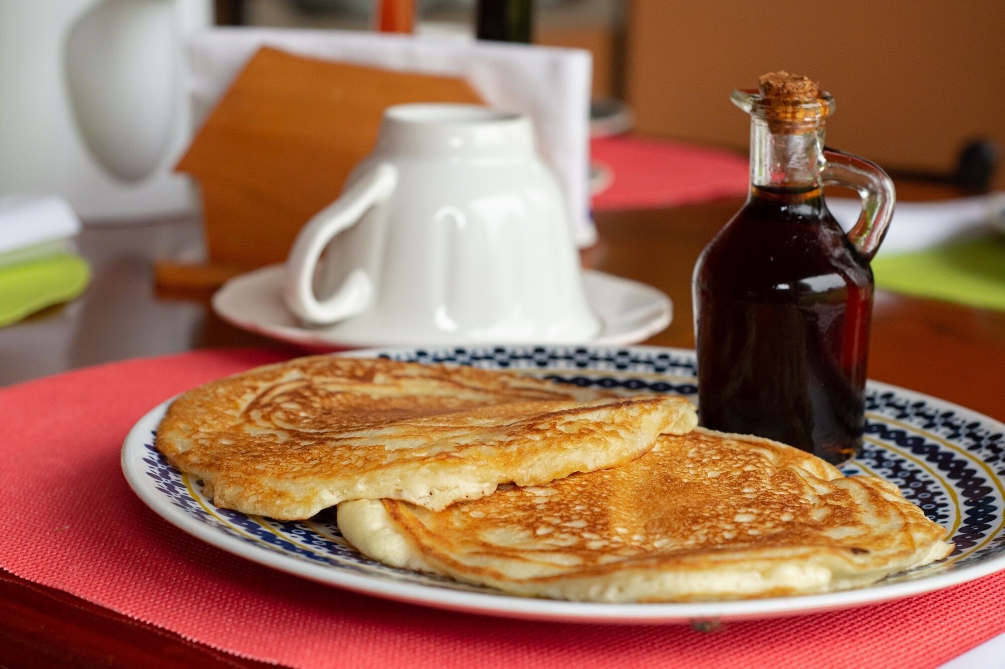 Une assiette avec deux crêpes et une bouteille de sirop, posée sur une table.