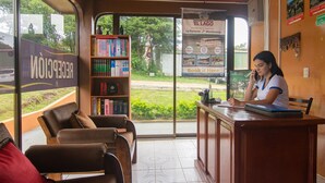 A reception area with a receptionist at a desk, a bookshelf, and a view of the outside. - Nafre House (Monteverde)