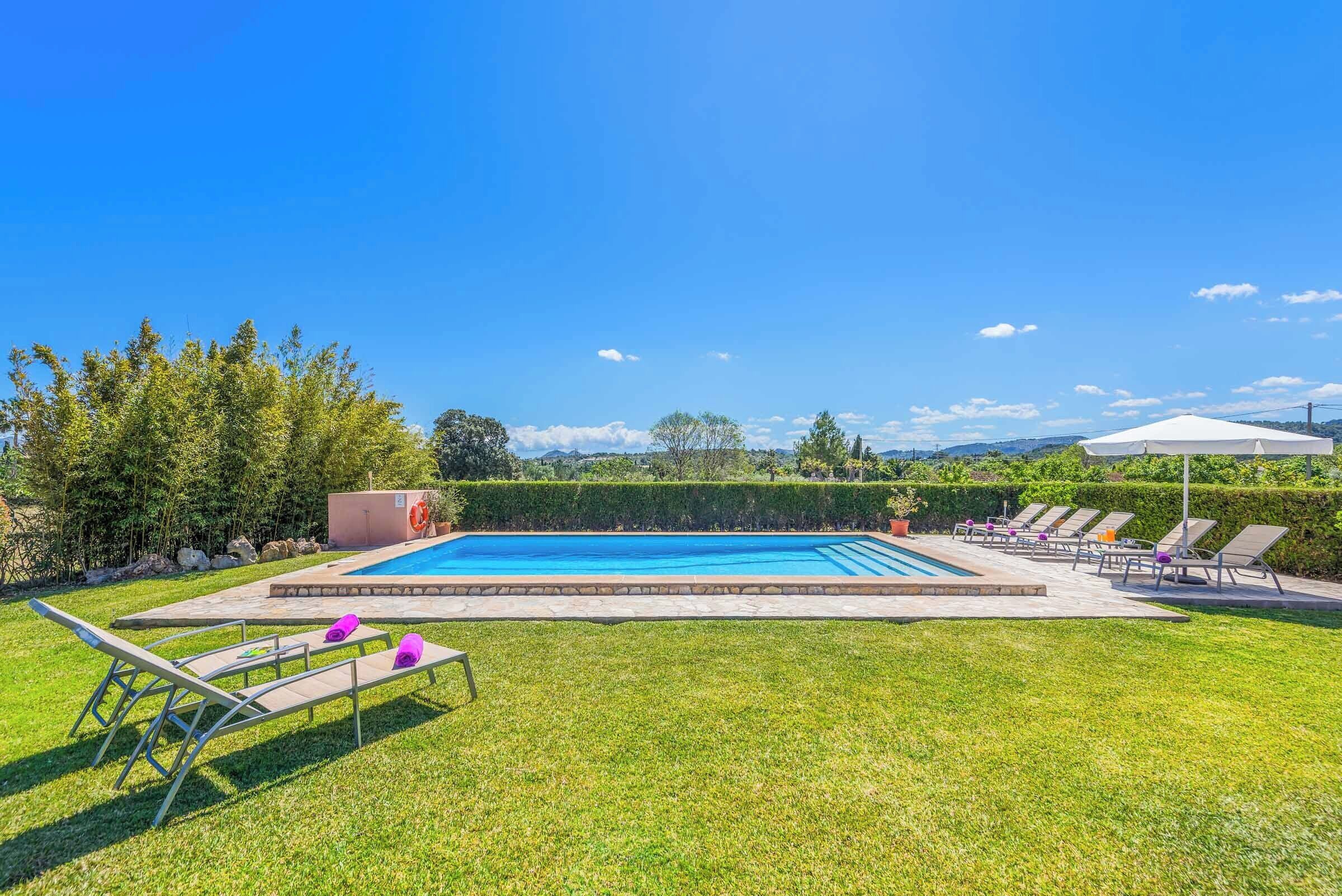 A rectangular swimming pool with a stone border, surrounded by a well-maintained lawn and several lounge chairs.