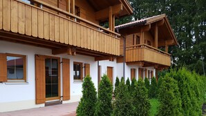 Una cabaña de madera con balcón, paredes blancas y un jardín con árboles de coníferas.