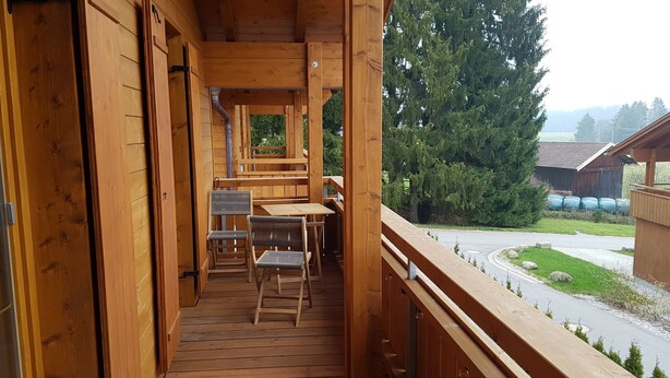 Un balcón de madera con una mesa y sillas, con vista a una calle y vegetación.