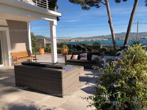 An outdoor seating area with wicker furniture and potted plants, overlooking a coastal landscape.